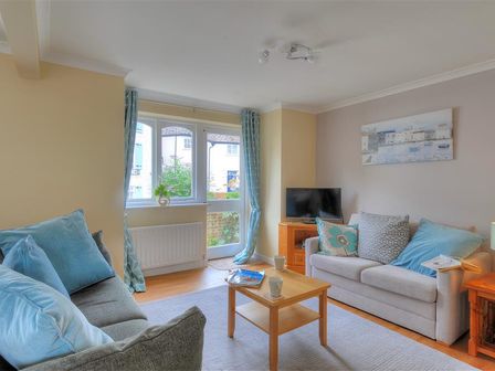 A sitting room with two sofas a wooden coffee table a TV and a window with curtains at The Old Bakehouse in Lyme Regis