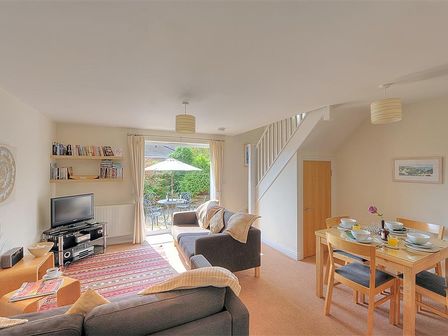 A living room with sofas a television a dining table set for four and a view of a patio at 1 Coppers Knapp in Lyme Regis