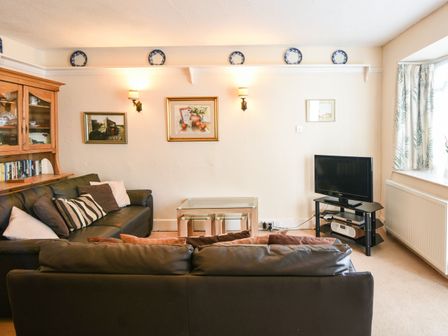 A living room with two dark sofas a glass coffee table a television on a stand and a wooden cabinet at Okanagan in Lyme Regis