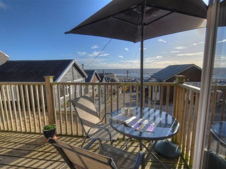 A wooden balcony with a table and chairs under an umbrella overlooking houses and the sea at St Anton in Lyme Regis