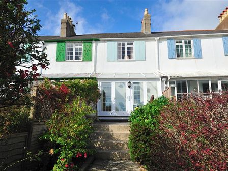 A row of terraced houses with green blue and light blue shutters and a garden with bushes and steps leading to white doors at Windwhistle in Lyme Regis