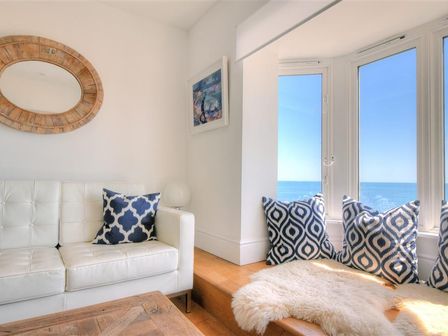 A white sofa with patterned pillows a wooden coffee table and a window seat with pillows and a sheepskin at Seahorse in Lyme Regis