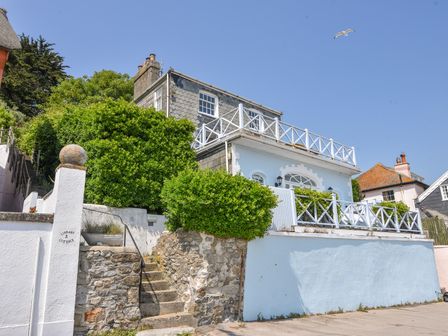 Exterior of a two story house with white railings and stone steps surrounded by greenery at 3 Argyle House in Lyme Regis