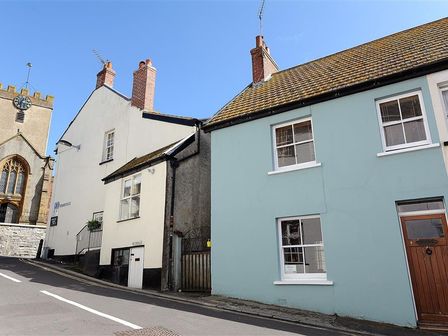 A street with pastel colored houses and a church with a clock tower at Bedrock in Lyme Regis