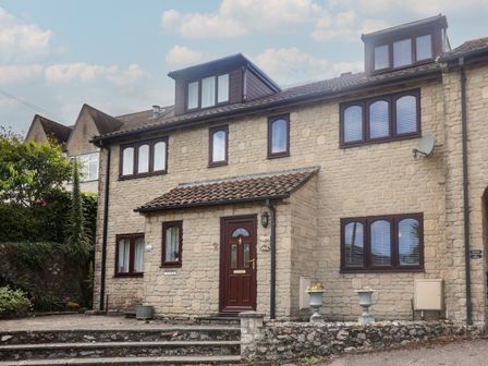 A stone house with brown framed windows and a brown door with steps and plants at 2 Kersbrook Gardens Lyme Regis