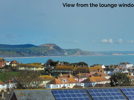 View of rooftops with solar panels and a coastal landscape with cliffs and the sea in the background at Upper Seascape in Lyme Regis