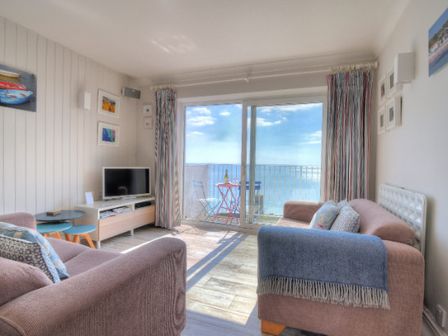 A living room with two sofas a television and a balcony overlooking the sea at 9 Bay View Court in Lyme Regis