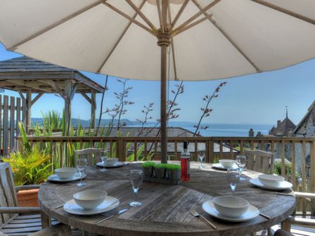 An outdoor wooden dining table set with bowls glasses and cutlery under a large umbrella with sea view at 4 Coram Court in Lyme Regis