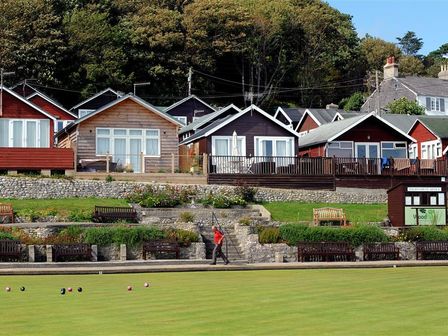 Houses behind a lawn bowls green with benches and gardens at 8 Bowling Green Chalets in Lyme Regis