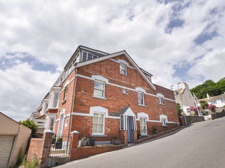 A red brick house with white window frames on a sloped street at The Lookout in Lyme Regis