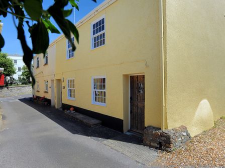 A yellow two story building with white framed windows and a wooden door on a paved street at 4 5 Georges Square in Lyme Regis