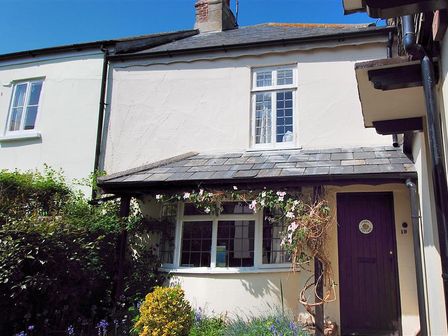 The exterior of a cream colored cottage with a slate roof purple door and flowering plants at Ivy Cottage in Lyme Regis