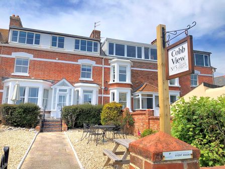 A brick house with white framed windows and a patio area with tables and chairs at 2 Cobb View in Lyme Regis