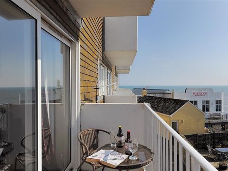 A balcony with a table and chairs overlooking the sea and buildings at 4 Bay View Court in Lyme Regis