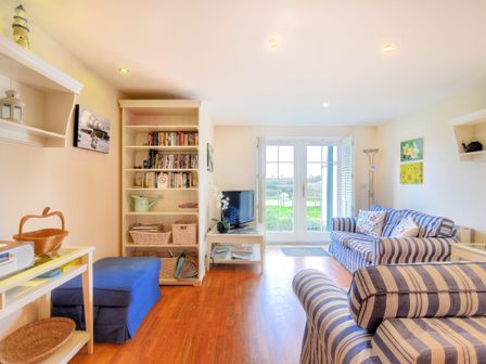 A living room with striped sofas a bookshelf and a small TV near glass doors at 2 Buckfields Lyme Regis