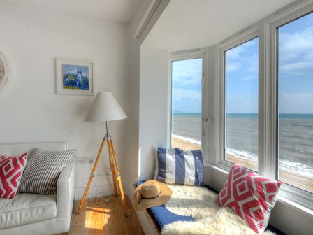 A corner seating area with striped and patterned cushions a floor lamp and a window seat overlooking the beach and sea at Starfish in Lyme Regis