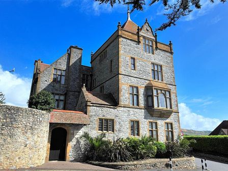 An old stone building with multiple windows and a tower under a blue sky at 7 Coram Tower in Lyme Regis