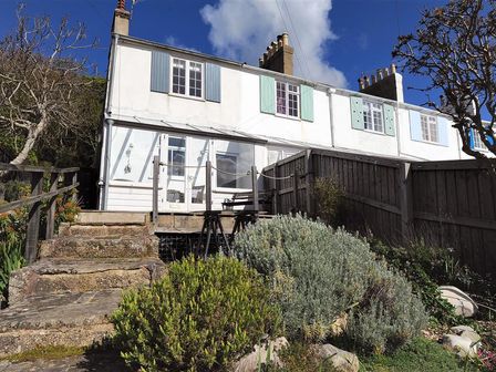 A white two-story house with blue and green shutters two chimneys stone steps leading to a patio with wooden fence and garden at 10 Cobb Terrace Lyme Regis