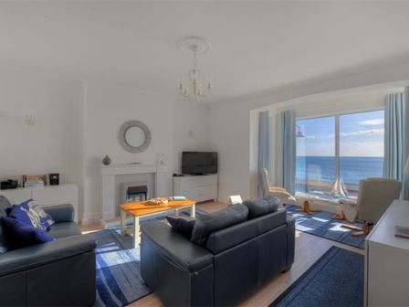 A living room with black leather sofas a wooden coffee table a fireplace a TV and large windows overlooking the sea at 2 Mareeba in Seaton