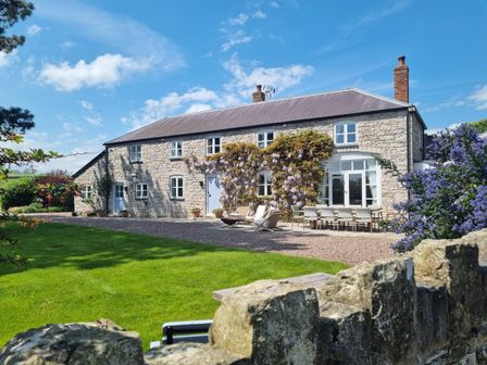 A stone house with outdoor seating and flowering plants in a garden at Ystrad Bach in Denbigh