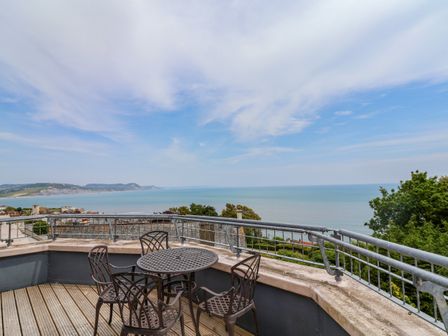 A balcony with a metal table and chairs overlooking the sea and coastline at The Penthouse in Lyme Regis
