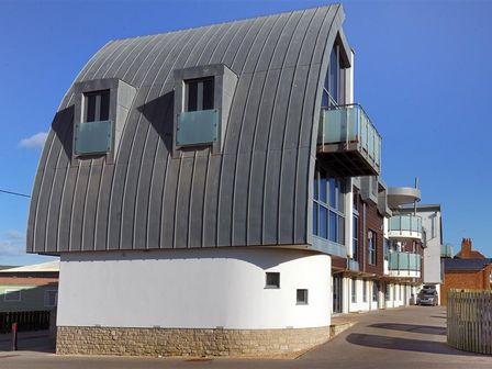 A modern building with curved metal roof and balconies at 8 Driftwood in West Bay