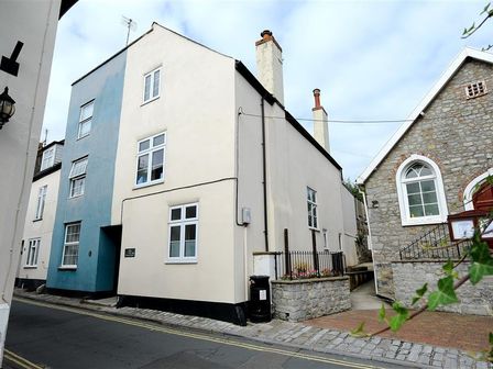 A street view of buildings including a blue and white house and a stone building with arched windows at Mermaid House in Lyme Regis