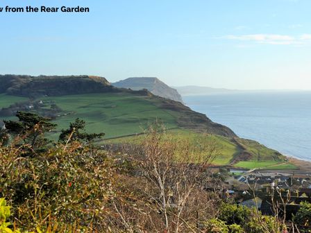 A coastal landscape with green hills and a village near the sea at Dolphins Leap in Charmouth