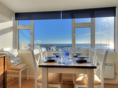 A dining room with a table set for six near large windows overlooking a marina and the sea at Halyards La Casa Lyme Regis