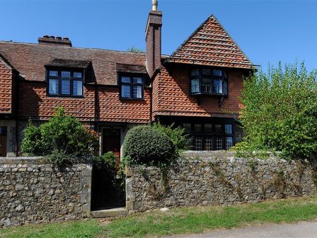 A traditional stone house with tiled roofs and black framed windows behind a stone wall with green bushes at 2 Old Home Farm in Rousdon