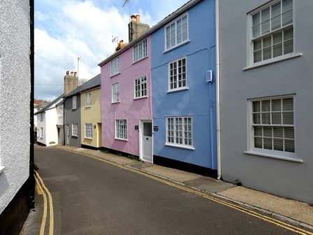 A narrow street with colorful terraced houses including blue, pink, yellow, and gray at Watersplash Cottage in Lyme Regis