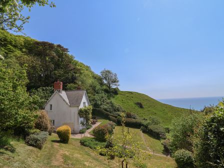 A cottage surrounded by greenery and a garden with a view of the sea at Lynch Cottage in Rousdon