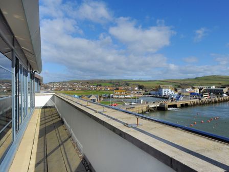 A balcony with a railing and glass doors overlooking a harbor and buildings at The Penthouse in West Bay