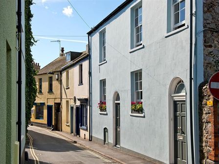 A narrow street with several houses including one with arched doors and flower boxes in Lyme Regis