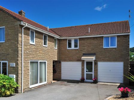 A two-story house with stone walls two white garage doors and a small front door at Bridge House Apartment in Charmouth
