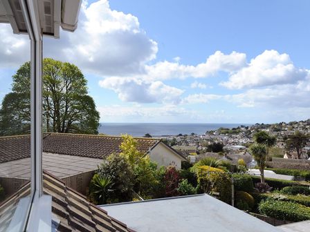 A coastal town view with rooftops trees and ocean under a cloudy sky at Sandpiper in Lyme Regis
