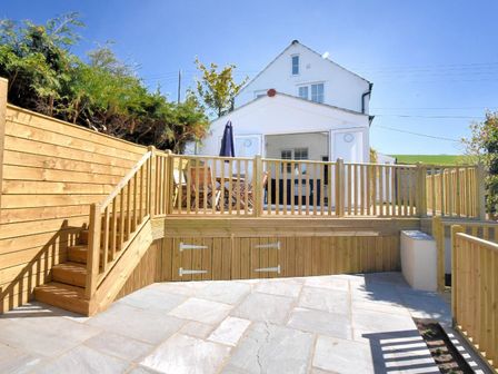 A backyard with wooden decking patio table chairs and umbrella next to a white house at Hillside Cottage in Uplyme