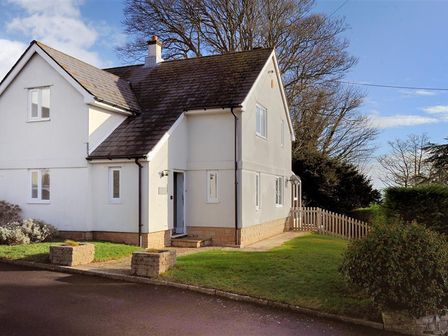 A two-story white house with a tiled roof a small front garden and a picket fence at High Cliff Cottage in Lyme Regis