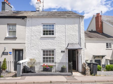 A street view of terraced cottages with white walls and a black iron fence at Nutwood in Charmouth