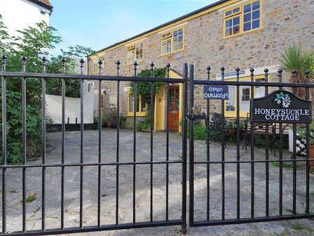 A stone cottage with yellow window frames and a black iron gate at Honeysuckle Cottage Lyme Regis