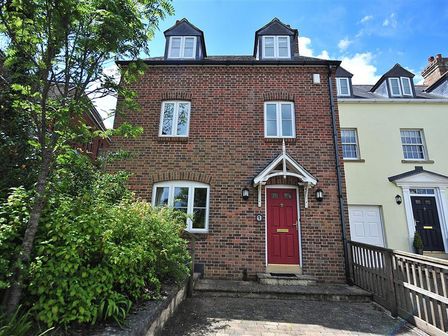 A brick townhouse with a red door and white-framed windows next to a yellow house with dormer windows at 1 Woodroffe Meadow Lyme Regis