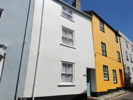 A street view of three adjoining houses painted blue white and yellow with windows and doors at Monmouth Cottage in Lyme Regis