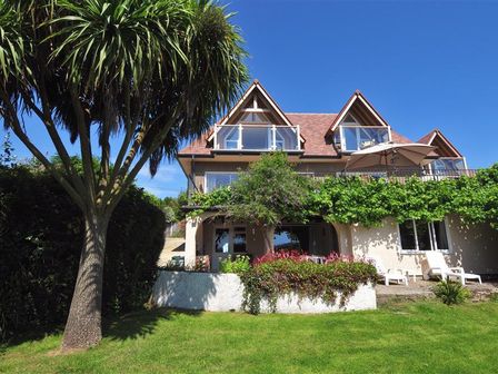 A two-story house with triangular roof windows a balcony a patio with chairs and greenery on a lawn at Willows in Charmouth