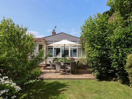 A garden patio with a table and chairs under an umbrella surrounded by shrubs at Little Ascot in Lyme Regis