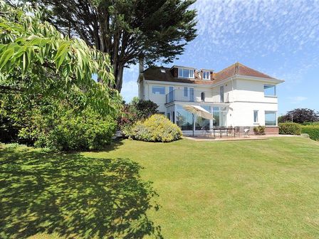 A two-story white house with a patio umbrella and outdoor furniture surrounded by a lawn and trees at Somerhill in Lyme Regis
