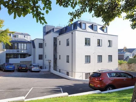 A parking lot with several cars in front of a multi-story white building with multiple windows and blue roof at Seashell in Lyme Regis