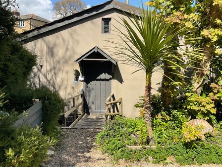 An entrance with a wooden door and small porch surrounded by plants and trees at The Sawmill in Beaminster