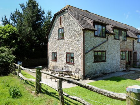 An outdoor patio area with a table and chairs next to a stone house with multiple windows at East Barn in Charmouth