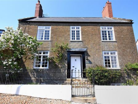 A stone house with white windows and a black gate surrounded by flowering bushes at Stone House in Charmouth