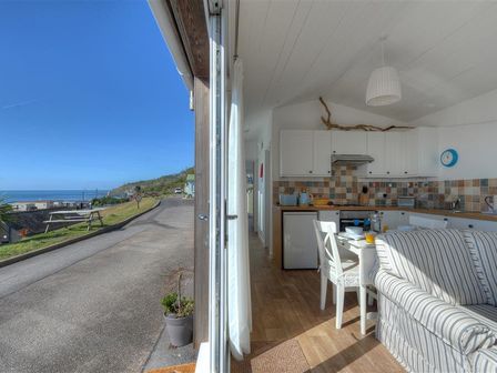 A kitchen and dining area with white cabinets and striped sofa at The Beach Hut in Lyme Regis